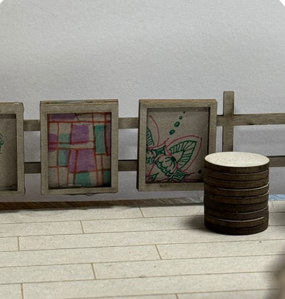 Scale model: a row of framed artworks by local makers along the fence.