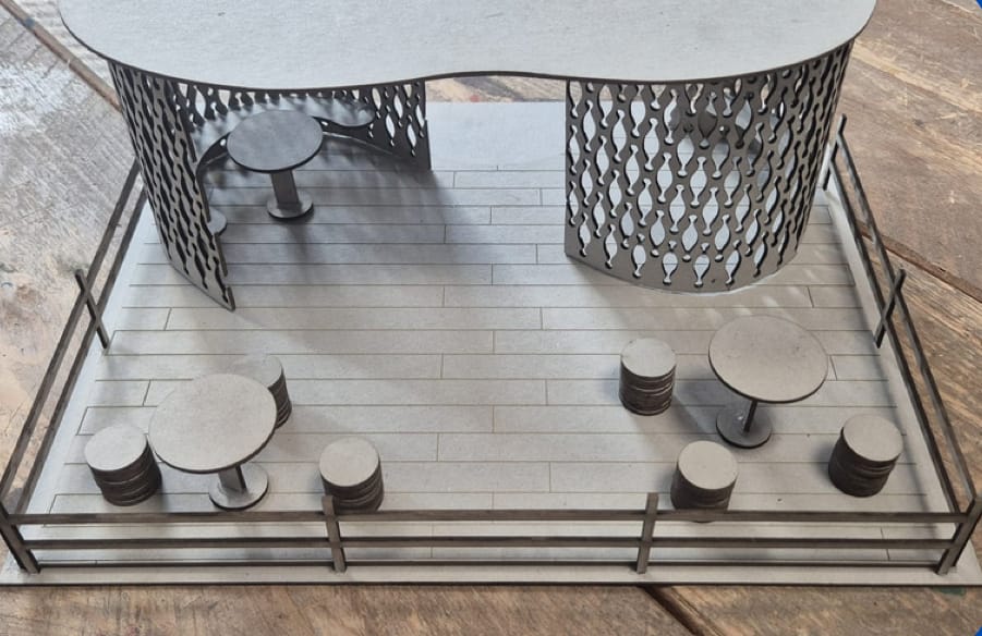 The whole scale model: rounded walls, roof and terrace with tables inside a fence.