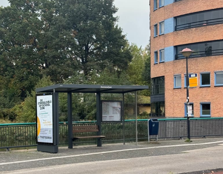 The Zonnewijzer bus stop as it is now: a glass shelter next to a brick apartment block.