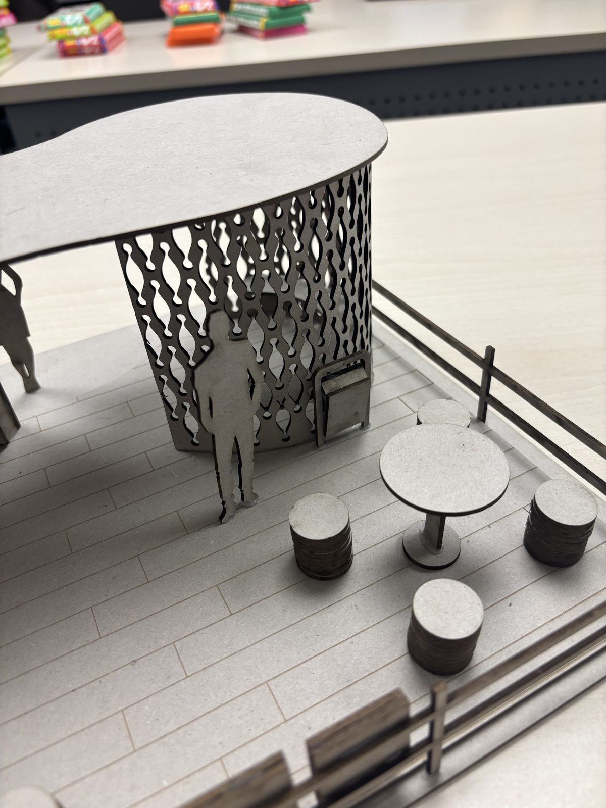 Scale model detail: seating and table under the curved, perforated wall.