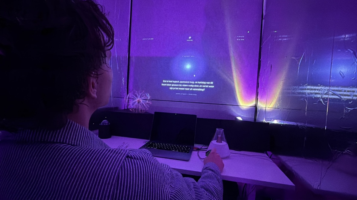A visitor seated at the desk in the dark purple chamber, facing the wall where Vendi projects its personal greeting.